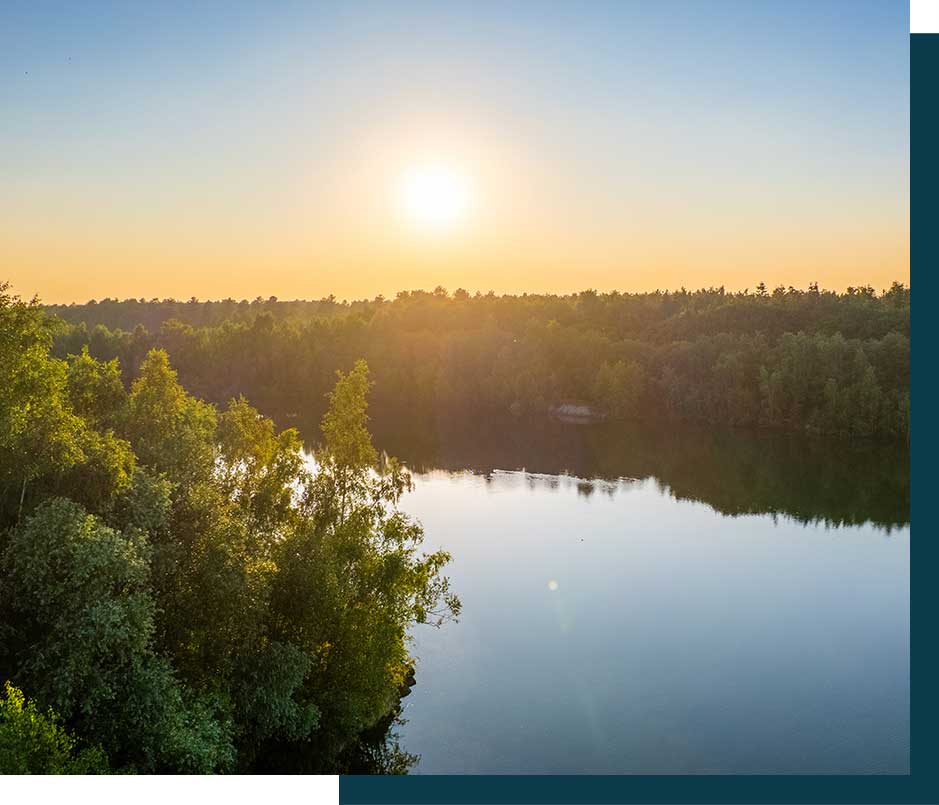 the tranquil beauty of a sunset over a still lake, bordered by a lush forest.